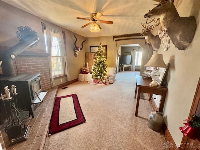 interior space with carpet flooring, a wood stove, and ceiling fan