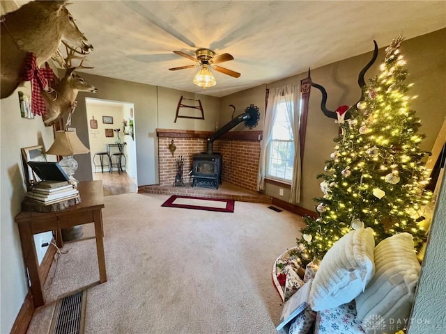 living room featuring carpet flooring, a wood stove, and ceiling fan