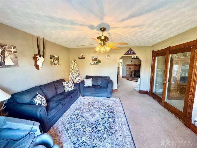 living room with carpet flooring, ceiling fan, a textured ceiling, and a brick fireplace