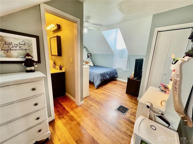 bedroom featuring light wood-type flooring, vaulted ceiling, ceiling fan, and connected bathroom