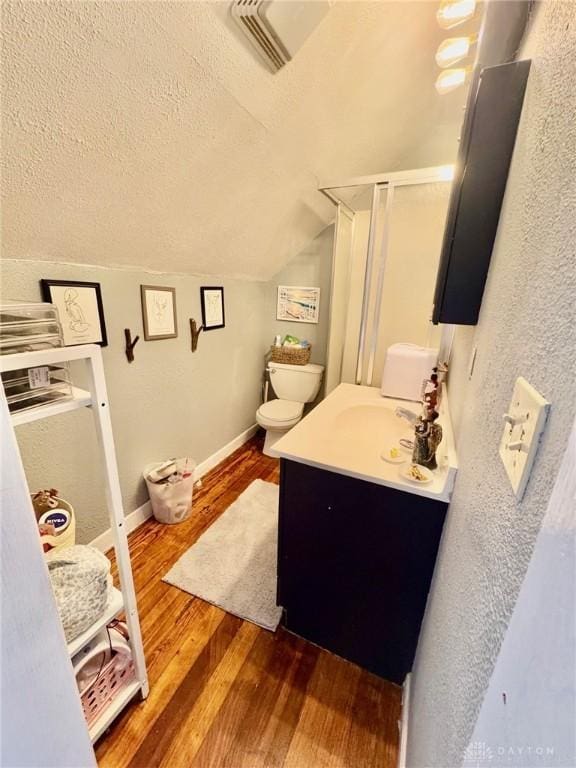 bathroom featuring hardwood / wood-style floors, a textured ceiling, vaulted ceiling, toilet, and vanity