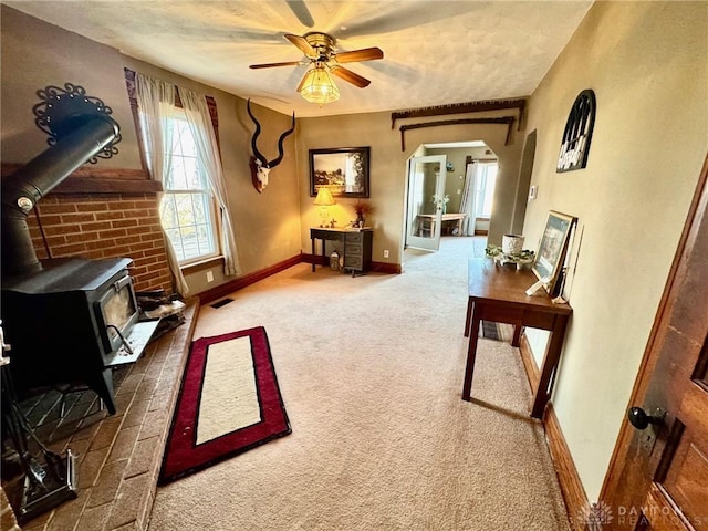 sitting room featuring carpet, ceiling fan, and a wood stove