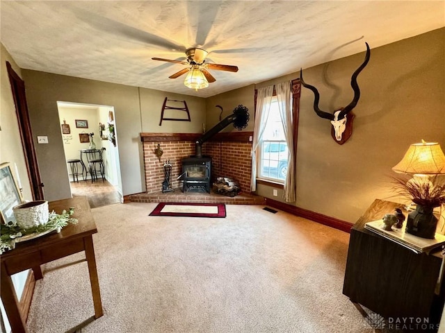 living room featuring ceiling fan, a textured ceiling, light carpet, and a wood stove