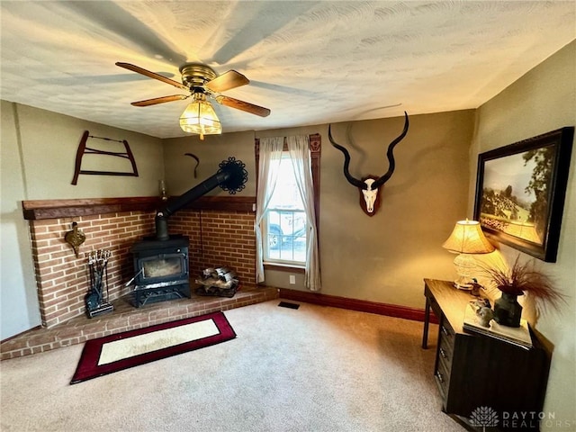 carpeted living room with ceiling fan, a textured ceiling, and a wood stove