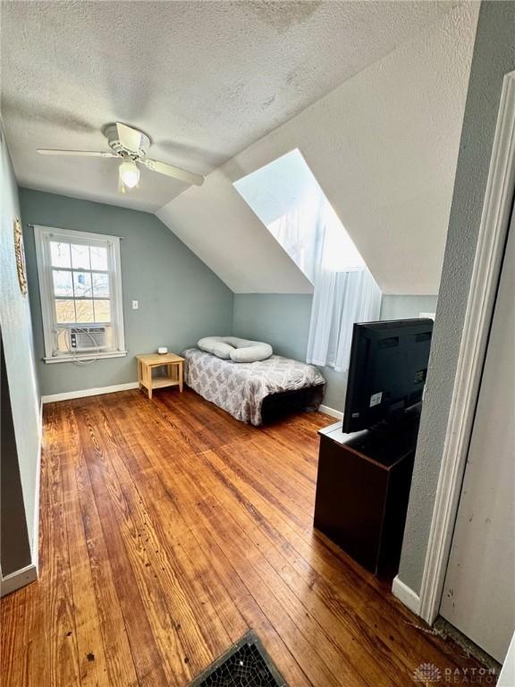 bedroom featuring ceiling fan, cooling unit, hardwood / wood-style floors, a textured ceiling, and vaulted ceiling