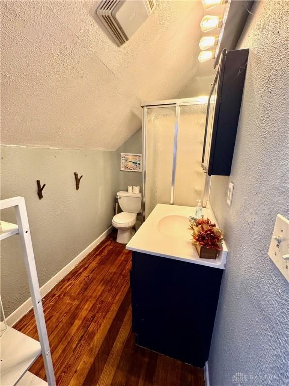 bathroom featuring hardwood / wood-style floors, vanity, a textured ceiling, vaulted ceiling, and toilet