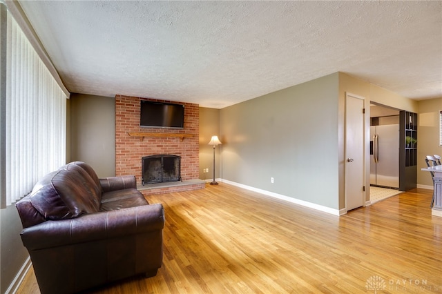 living room featuring a brick fireplace, light hardwood / wood-style floors, and a textured ceiling