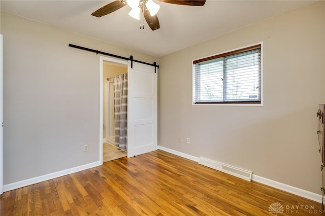 unfurnished bedroom featuring wood-type flooring, a barn door, ceiling fan, and a closet