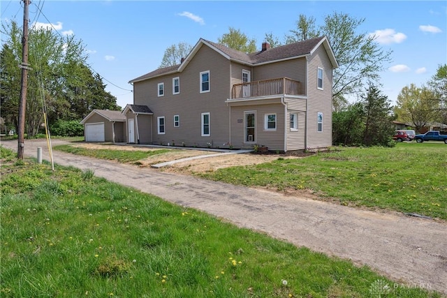 back of house featuring a chimney, a garage, a balcony, and a lawn