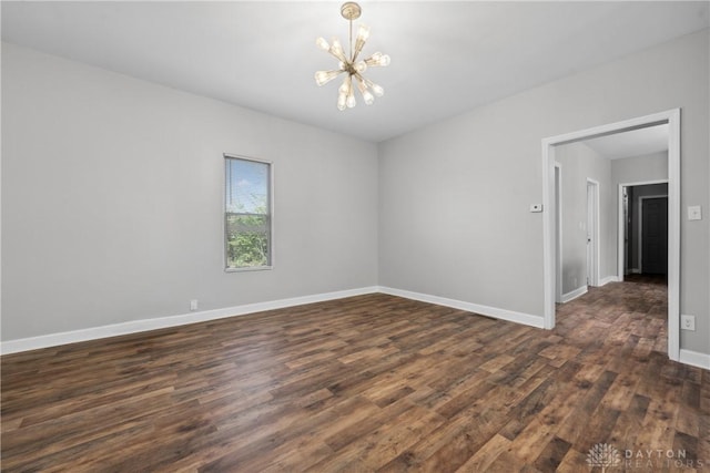 spare room with dark wood finished floors, baseboards, and a notable chandelier