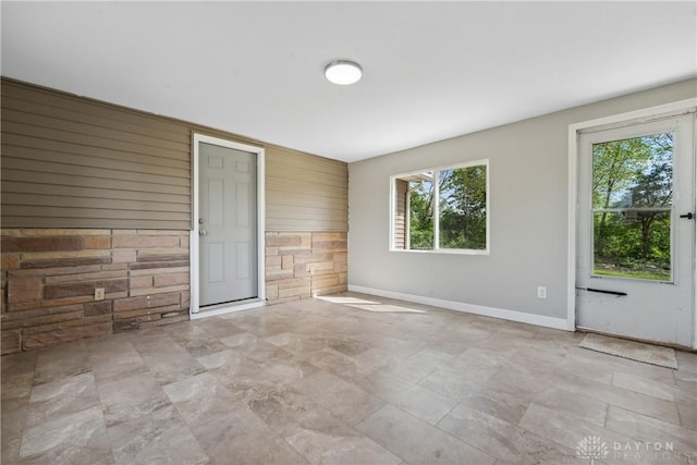 unfurnished room with wooden walls, baseboards, an accent wall, and a healthy amount of sunlight