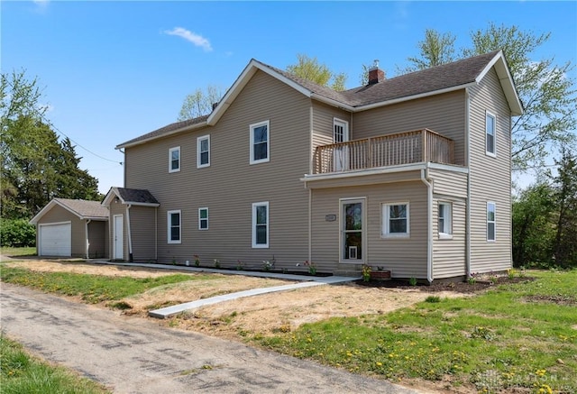 exterior space featuring a chimney, a garage, a lawn, a balcony, and an outdoor structure