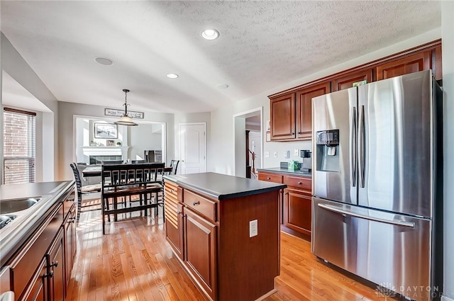 kitchen featuring a center island, hanging light fixtures, stainless steel fridge with ice dispenser, light hardwood / wood-style floors, and a textured ceiling