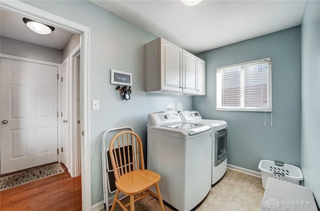 washroom featuring cabinets, washing machine and clothes dryer, and light hardwood / wood-style flooring