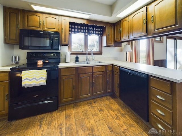 kitchen featuring black appliances, dark hardwood / wood-style flooring, kitchen peninsula, and sink