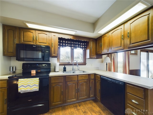 kitchen featuring black appliances, dark hardwood / wood-style flooring, kitchen peninsula, and sink