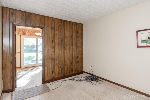 carpeted spare room featuring a textured ceiling and wood walls