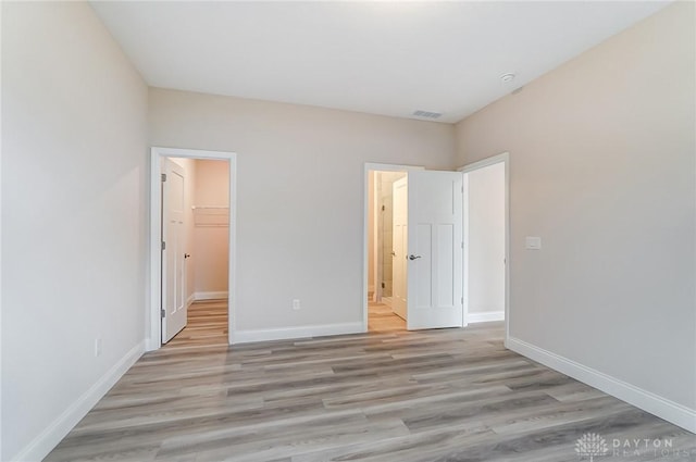 unfurnished bedroom with light wood-type flooring, a walk in closet, and a closet