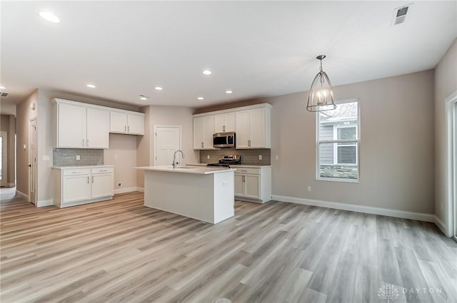 kitchen featuring a center island with sink, appliances with stainless steel finishes, a notable chandelier, light hardwood / wood-style floors, and white cabinetry