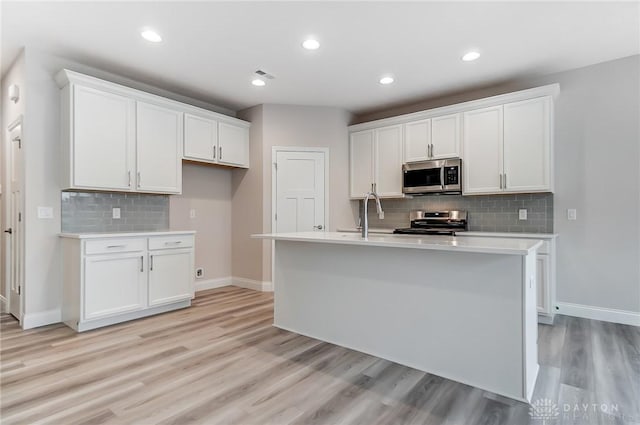 kitchen with white cabinets, a center island with sink, stainless steel appliances, and light hardwood / wood-style flooring