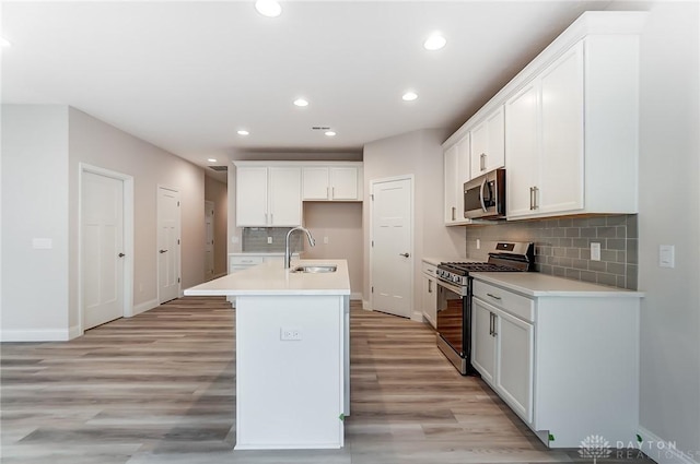 kitchen featuring appliances with stainless steel finishes, light wood-type flooring, sink, white cabinetry, and an island with sink