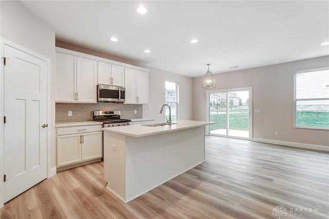 kitchen with stainless steel appliances, a kitchen island with sink, pendant lighting, light hardwood / wood-style floors, and white cabinetry