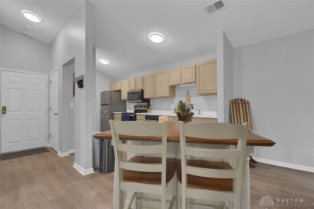 kitchen with light brown cabinets, lofted ceiling, stainless steel appliances, and light hardwood / wood-style flooring