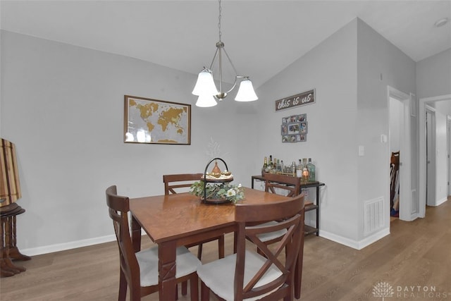 dining space featuring dark hardwood / wood-style flooring, an inviting chandelier, and vaulted ceiling