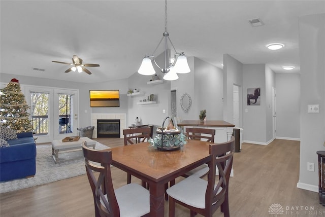 dining room featuring ceiling fan with notable chandelier, light hardwood / wood-style flooring, and a tiled fireplace