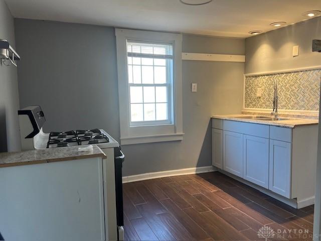 kitchen with baseboards, gas range, wood tiled floor, light countertops, and a sink