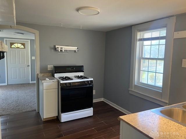 kitchen featuring dark wood-style floors, gas range gas stove, light countertops, white cabinets, and baseboards