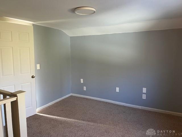 spare room featuring carpet flooring, vaulted ceiling, and baseboards