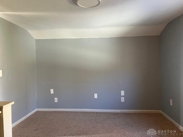 carpeted empty room with baseboards and vaulted ceiling