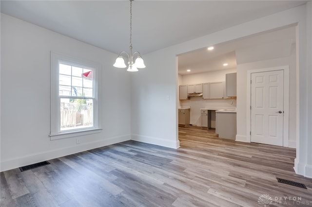 unfurnished dining area featuring an inviting chandelier and light hardwood / wood-style flooring