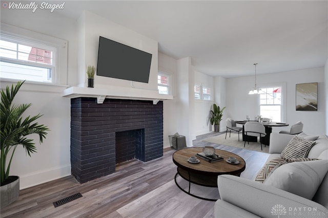 living room with hardwood / wood-style floors, an inviting chandelier, and a brick fireplace