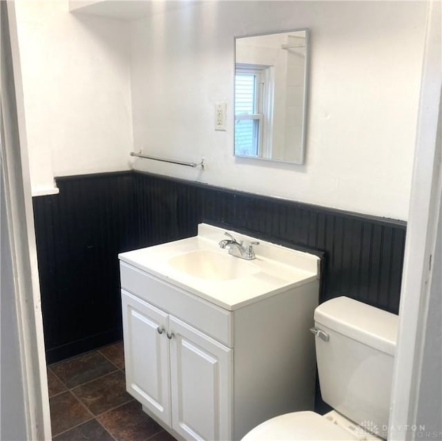 bathroom with wooden walls, vanity, and toilet