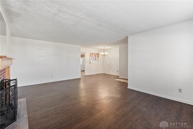 unfurnished living room with dark hardwood / wood-style flooring, a textured ceiling, an inviting chandelier, and a brick fireplace