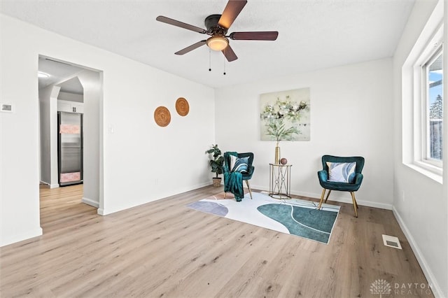 living area featuring light wood-style floors, visible vents, and ceiling fan