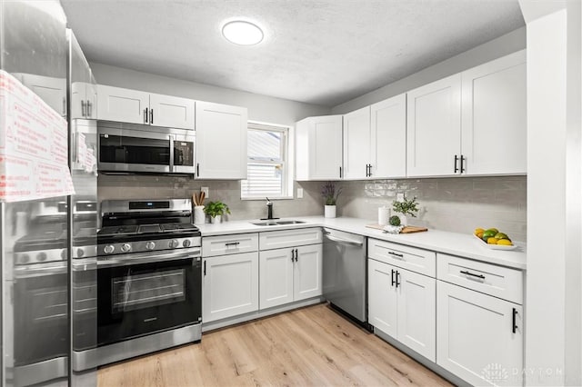 kitchen featuring white cabinetry, sink, light hardwood / wood-style floors, decorative backsplash, and appliances with stainless steel finishes