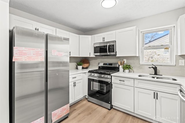 kitchen featuring appliances with stainless steel finishes, light countertops, light wood-style floors, white cabinetry, and a sink