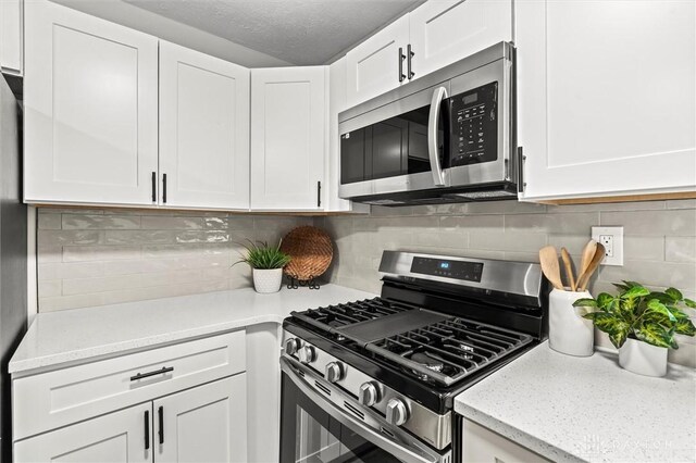 kitchen featuring decorative backsplash, white cabinets, light stone counters, and appliances with stainless steel finishes