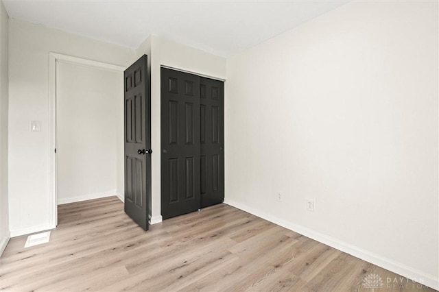 unfurnished bedroom featuring light wood-type flooring, a closet, and baseboards