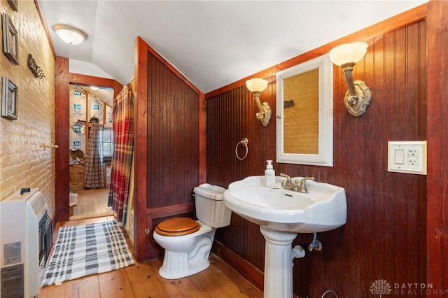 bathroom with wood-type flooring, vaulted ceiling, heating unit, and toilet