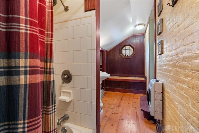 bathroom featuring heating unit, shower / tub combo, vaulted ceiling, brick wall, and hardwood / wood-style floors