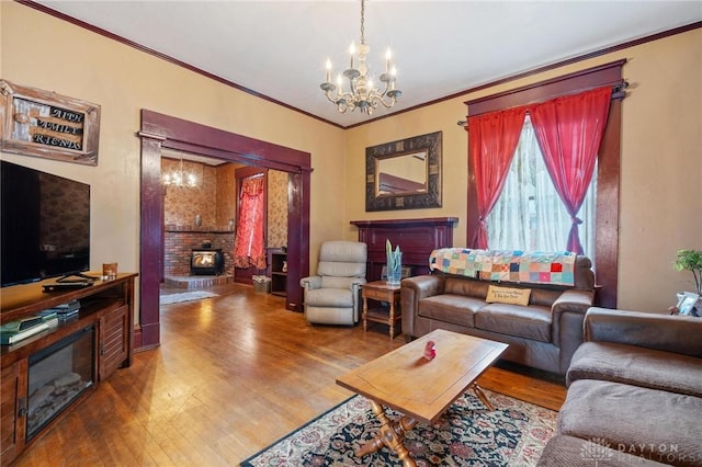 living room with wood-type flooring, ornamental molding, a fireplace, and an inviting chandelier