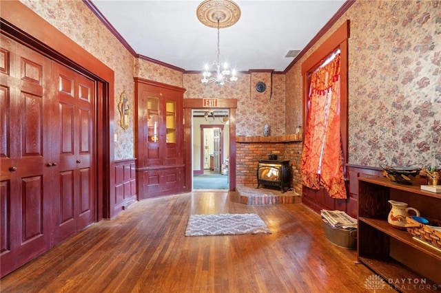 foyer featuring ornamental molding, hardwood / wood-style floors, a wood stove, and a notable chandelier