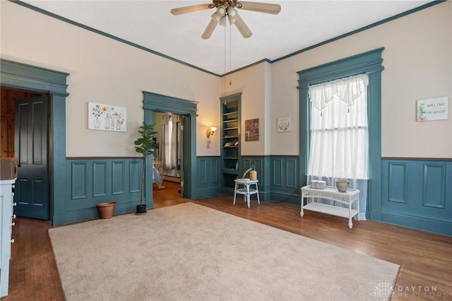 living area with a baseboard heating unit, ornamental molding, dark hardwood / wood-style floors, and ceiling fan