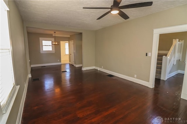 empty room featuring dark hardwood / wood-style flooring, ceiling fan with notable chandelier, and a textured ceiling