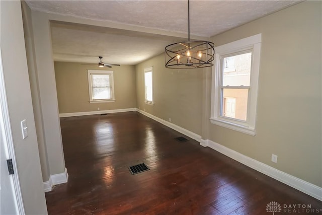 unfurnished dining area with ceiling fan with notable chandelier, dark hardwood / wood-style flooring, and a textured ceiling