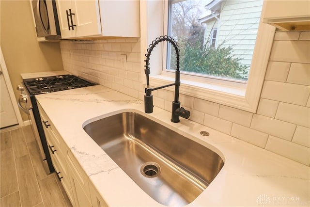 room details featuring sink, appliances with stainless steel finishes, tasteful backsplash, light hardwood / wood-style floors, and white cabinetry